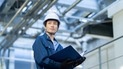 Construction worker in hard hat and blue uniform holding clipboard in industrial facility