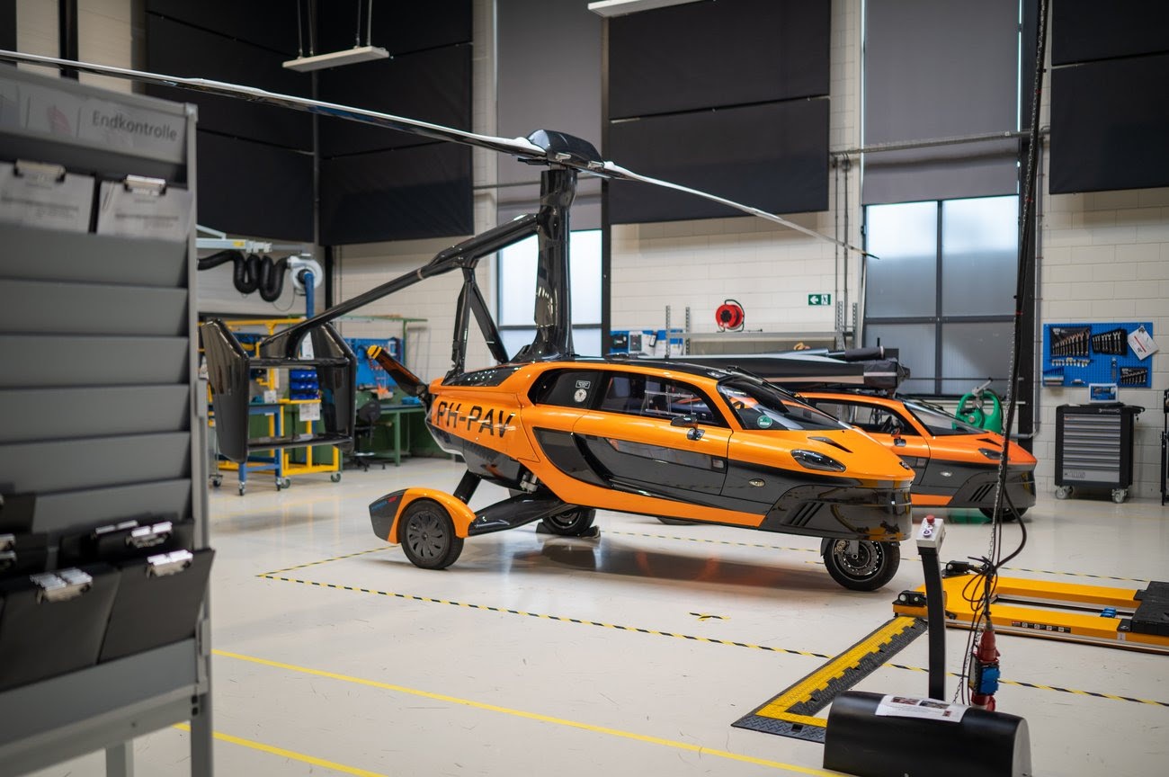 Orange and black hybrid flying car with rotor blade in industrial workshop hangar