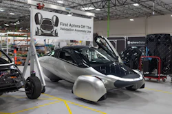 Aptera three-wheeled electric vehicle on display at manufacturing facility with validation assembly line banner