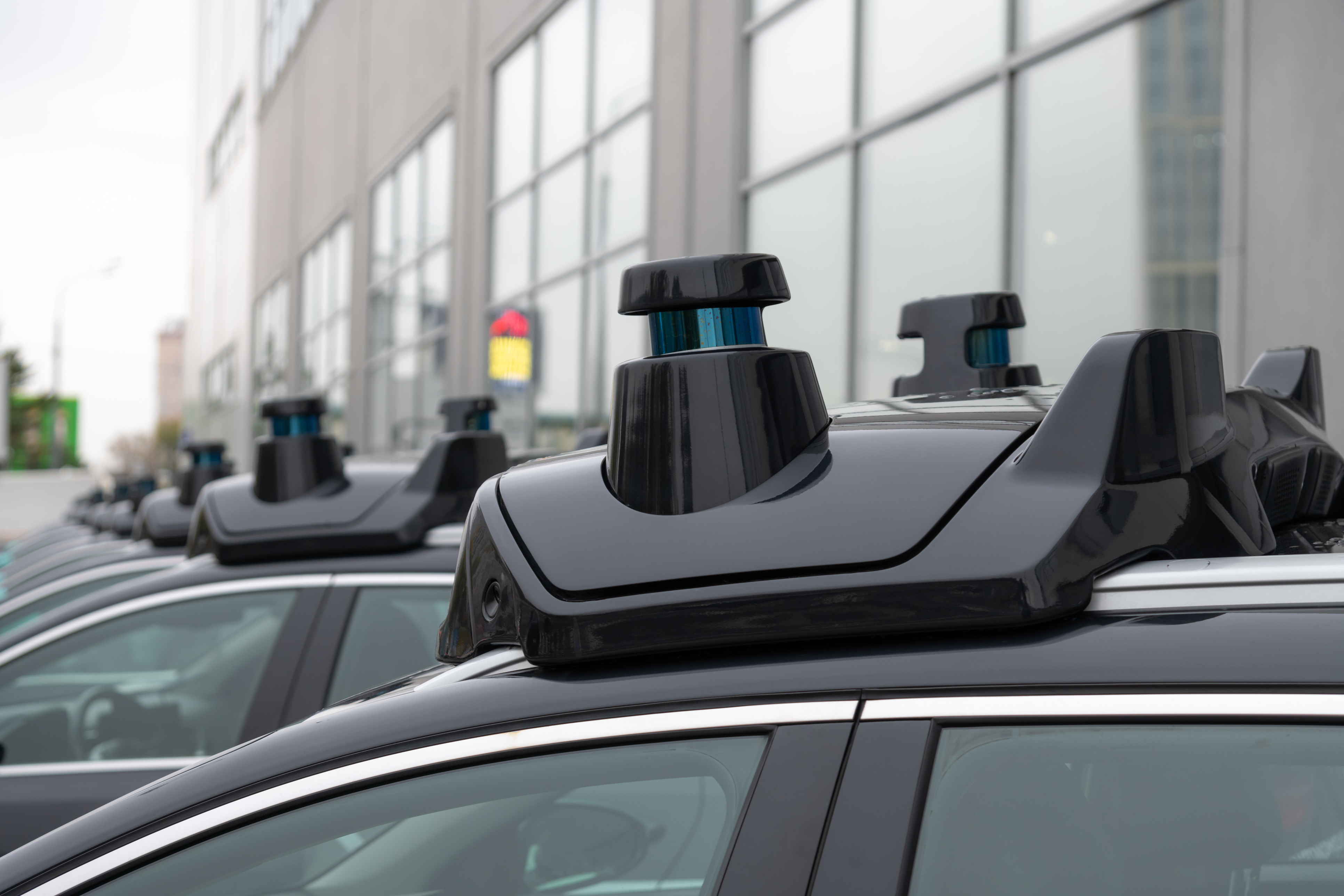 Row of vehicles with black roof racks and cargo carriers parked on urban street with modern building