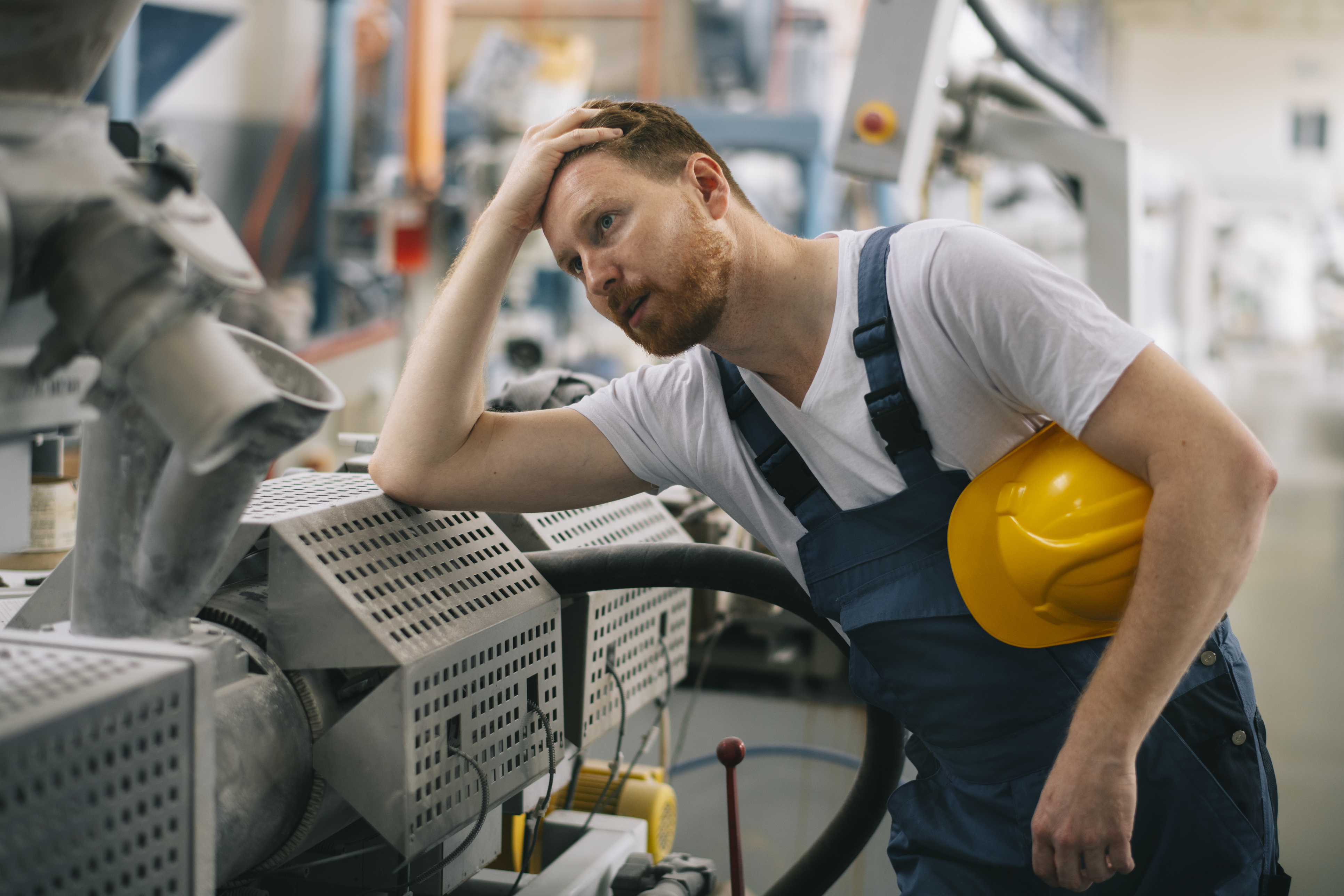 Male factory worker in hard hat inspecting industrial machinery in manufacturing facility