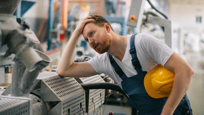 Male factory worker in hard hat inspecting industrial machinery in manufacturing facility