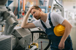 Male factory worker in hard hat inspecting industrial machinery in manufacturing facility