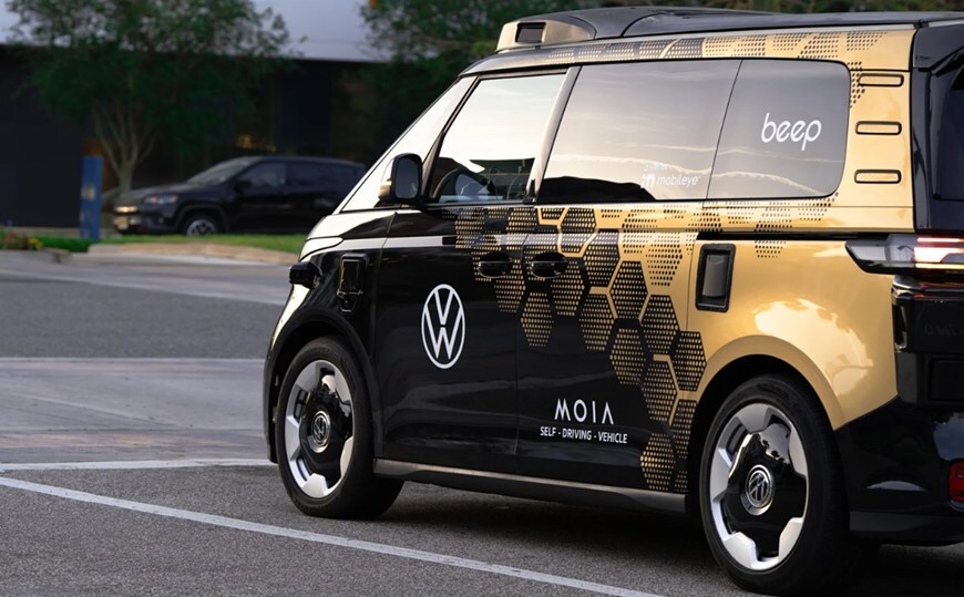 Gold and black Volkswagen ID. Buzz self-driving vehicle with Beep and Moia branding on a city street