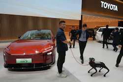 Red Toyota electric vehicle displayed at showroom event with robotic dog demonstration and attendees in modern facility