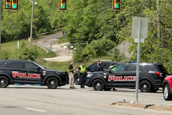 Police officers conducting traffic stop on street with multiple patrol vehicles and traffic lights visible