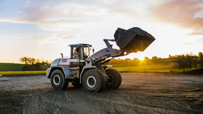 Wheel loader with raised bucket on rural road at sunset with green fields in background