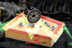 Automotive maintenance kit with oil filter, air filter, and spark plugs displayed on yellow packaging in engine bay