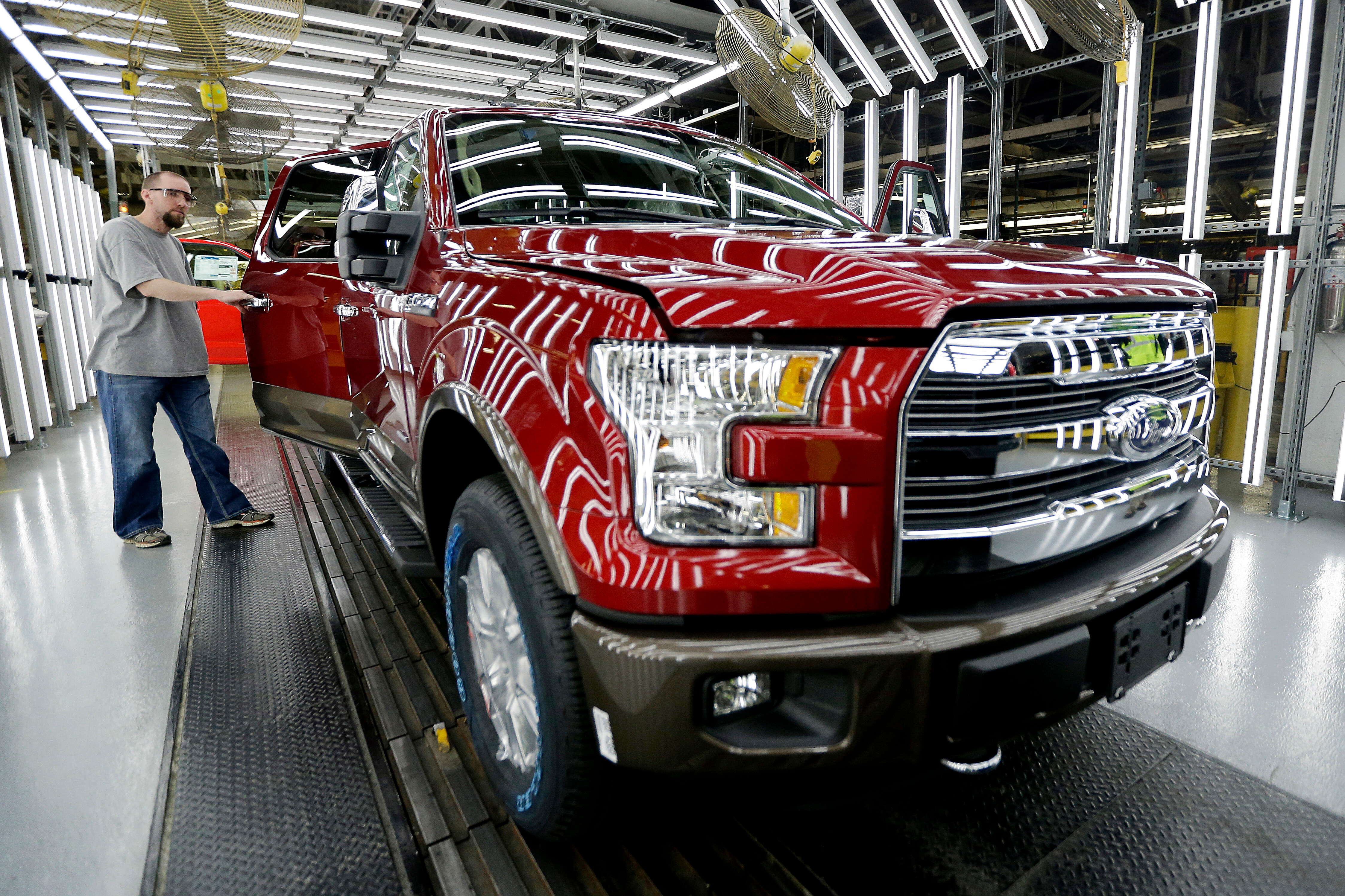 Red Ford F-150 truck on assembly line with worker in manufacturing facility