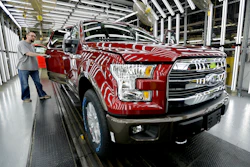 Red Ford F-150 truck on assembly line with worker in manufacturing facility