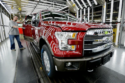 Red Ford F-150 truck on assembly line with worker in manufacturing facility
