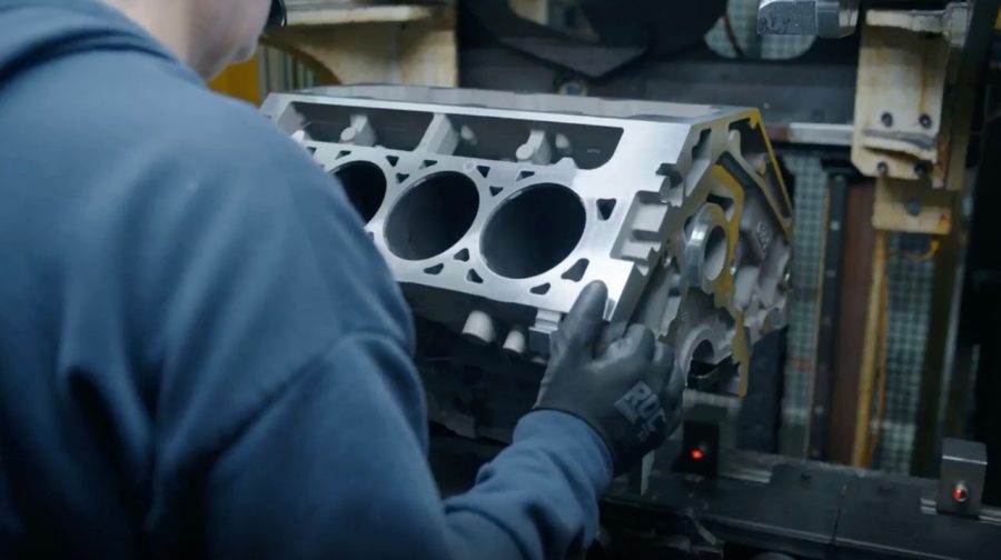 Technician inspecting aluminum engine block with cylinder openings in automotive workshop