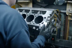 Technician inspecting aluminum engine block with cylinder openings in automotive workshop