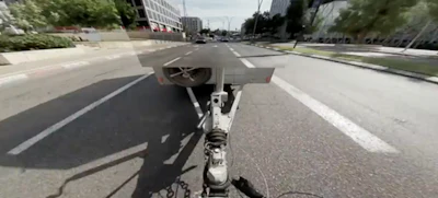 First-person view from bicycle handlebars on urban street with buildings and traffic ahead