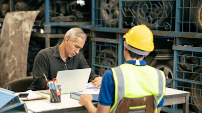 Supervisor reviewing documents with construction worker at industrial facility workstation