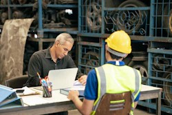 Supervisor reviewing documents with construction worker at industrial facility workstation