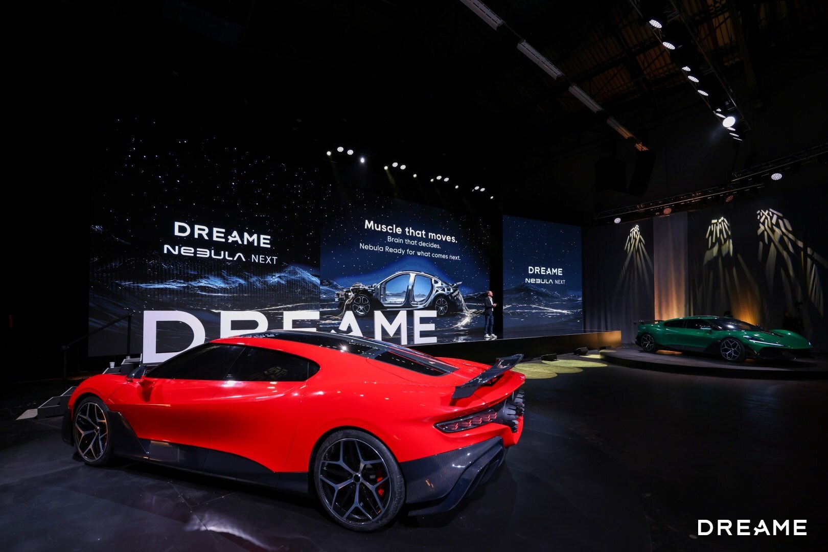 Red sports car displayed at DREAME automotive exhibition with branded signage and green vehicle in background