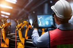 Factory worker in hard hat monitoring industrial robotic arms with tablet displaying production analytics and performance metrics