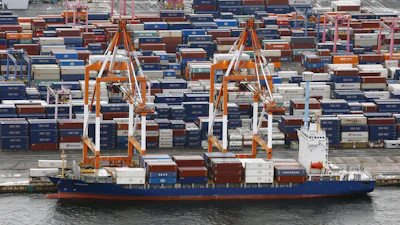 Cargo ship docked at container port with stacked shipping containers and orange loading cranes