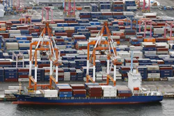 Cargo ship docked at container port with stacked shipping containers and orange loading cranes
