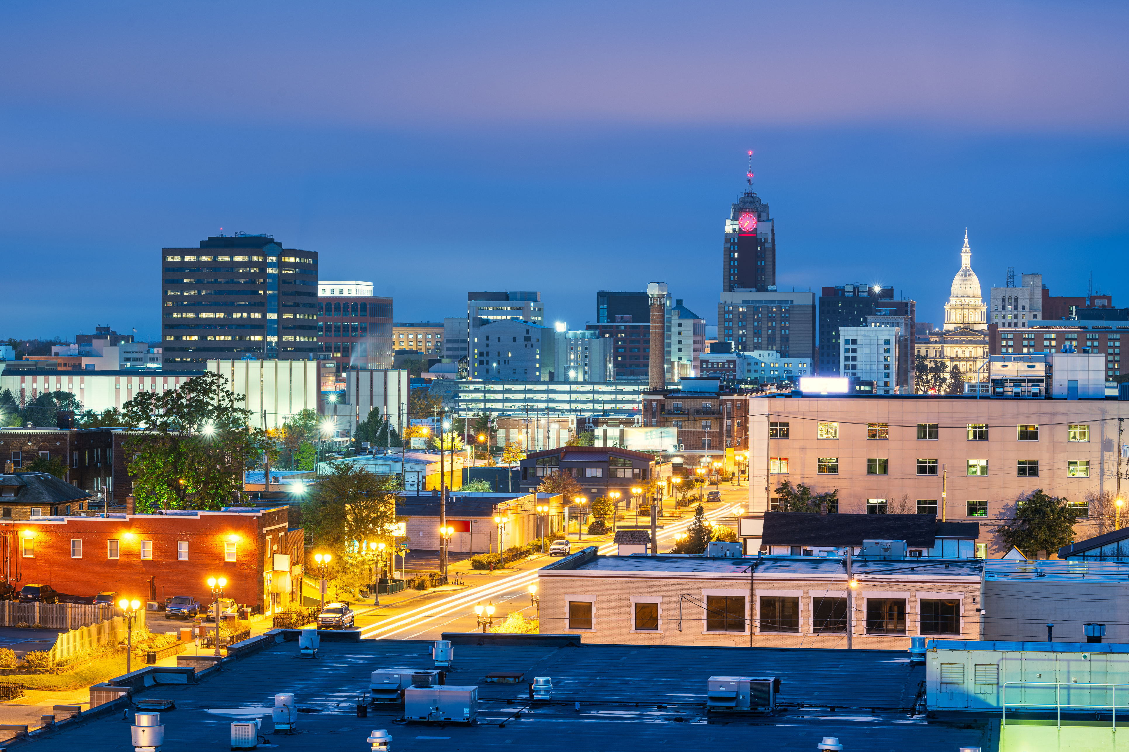 Urban skyline at twilight with illuminated buildings, street lights, and capitol dome in background