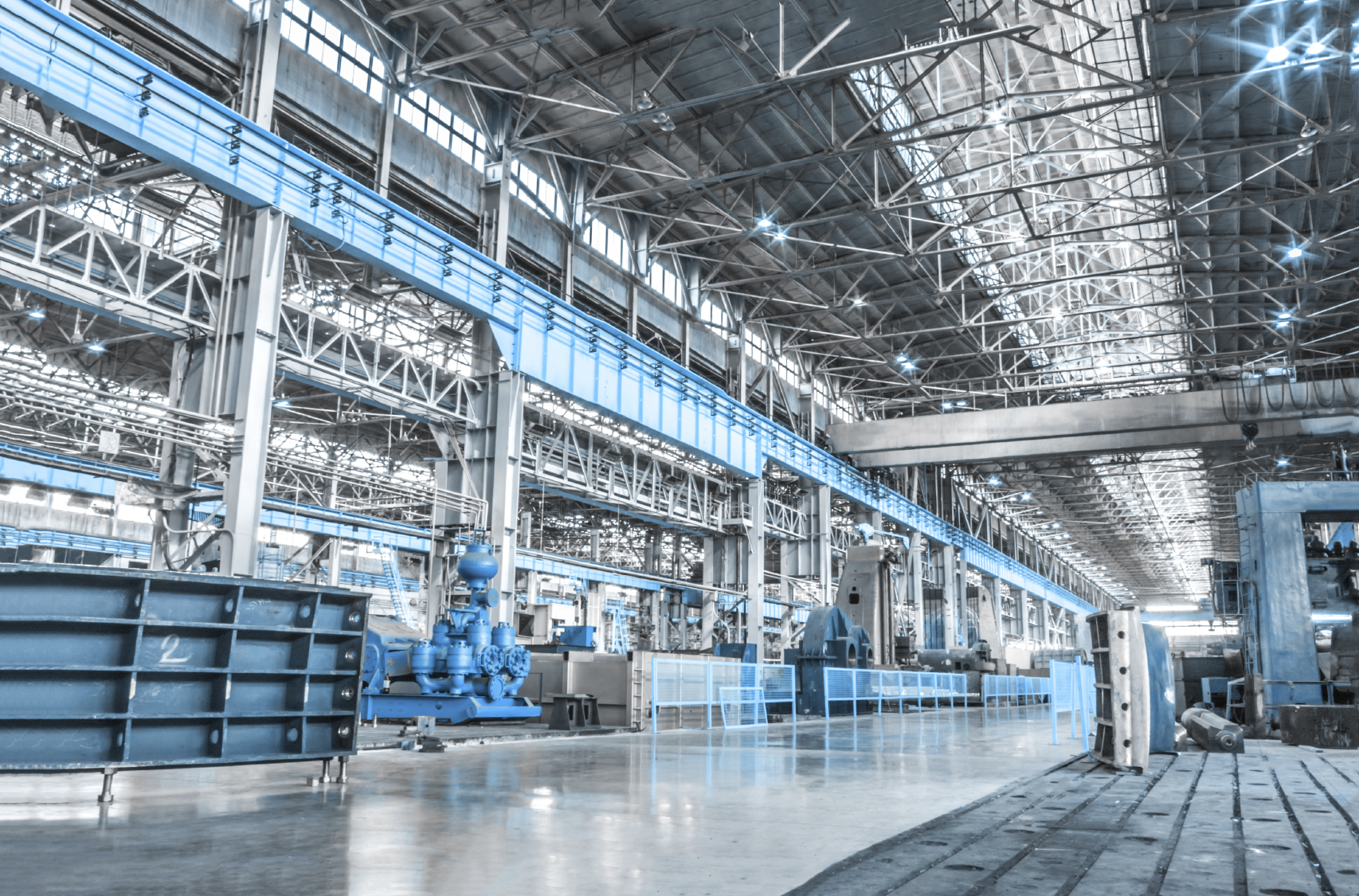 Spacious industrial factory floor with blue machinery, steel framework, and bright overhead lighting in a modern manufacturing facility