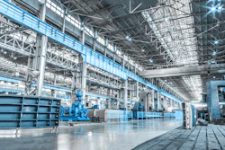 Spacious industrial factory floor with blue machinery, steel framework, and bright overhead lighting in a modern manufacturing facility