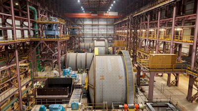 Industrial aerospace manufacturing facility with large cylindrical spacecraft components and overhead cranes in assembly bay