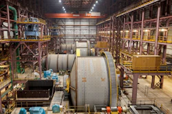 Industrial aerospace manufacturing facility with large cylindrical spacecraft components and overhead cranes in assembly bay