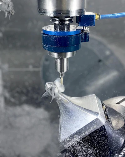 CNC milling machine with blue spindle head cutting a white metal workpiece with coolant spray