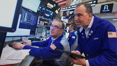 Traders monitor financial data at NYSE trading floor with multiple screens and American flags visible