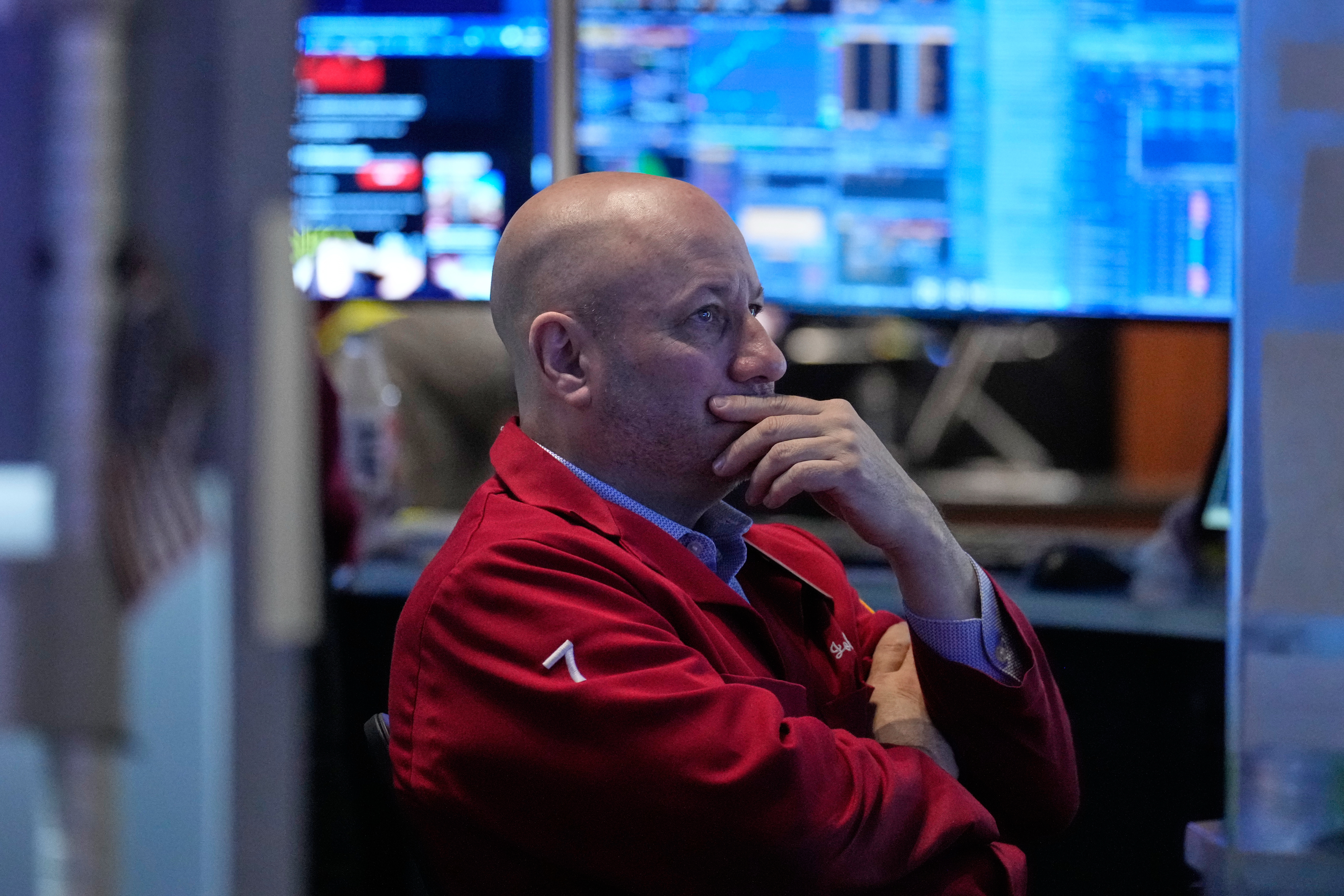Professional man in red jacket contemplating at computer workstation with multiple monitors