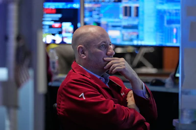Professional man in red jacket contemplating at computer workstation with multiple monitors