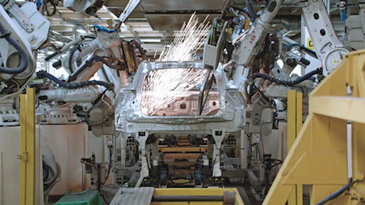 Robotic welding arms performing assembly on vehicle body in automotive manufacturing facility