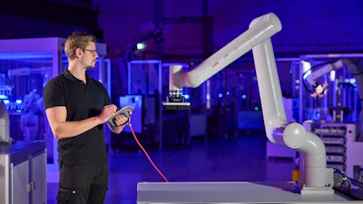 Technician operating white robotic arm with red controller in blue-lit industrial facility