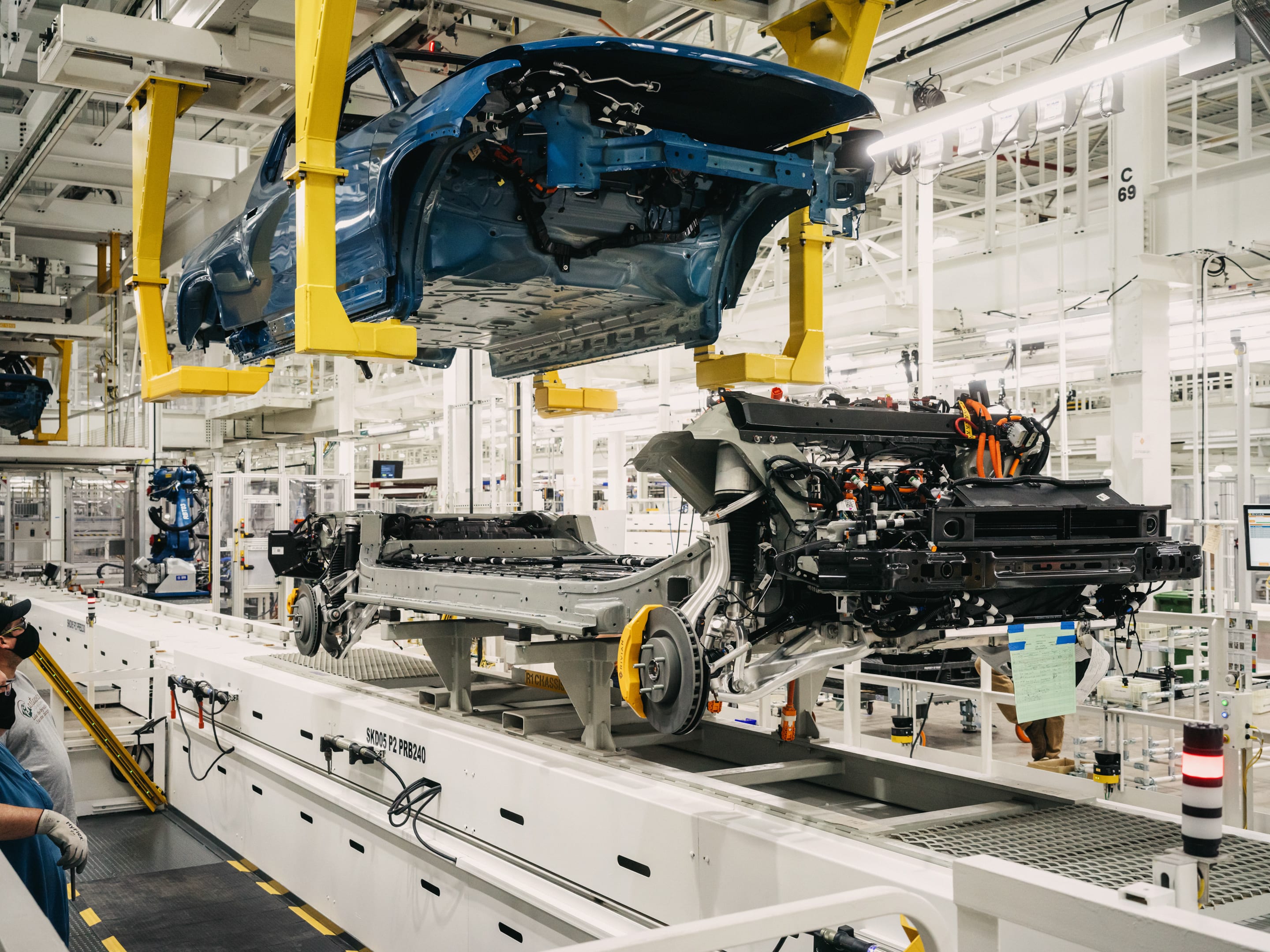 Blue car body suspended on assembly line with engine and chassis components during manufacturing