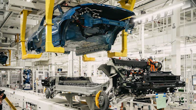 Blue car body suspended on assembly line with engine and chassis components during manufacturing