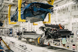 Blue car body suspended on assembly line with engine and chassis components during manufacturing