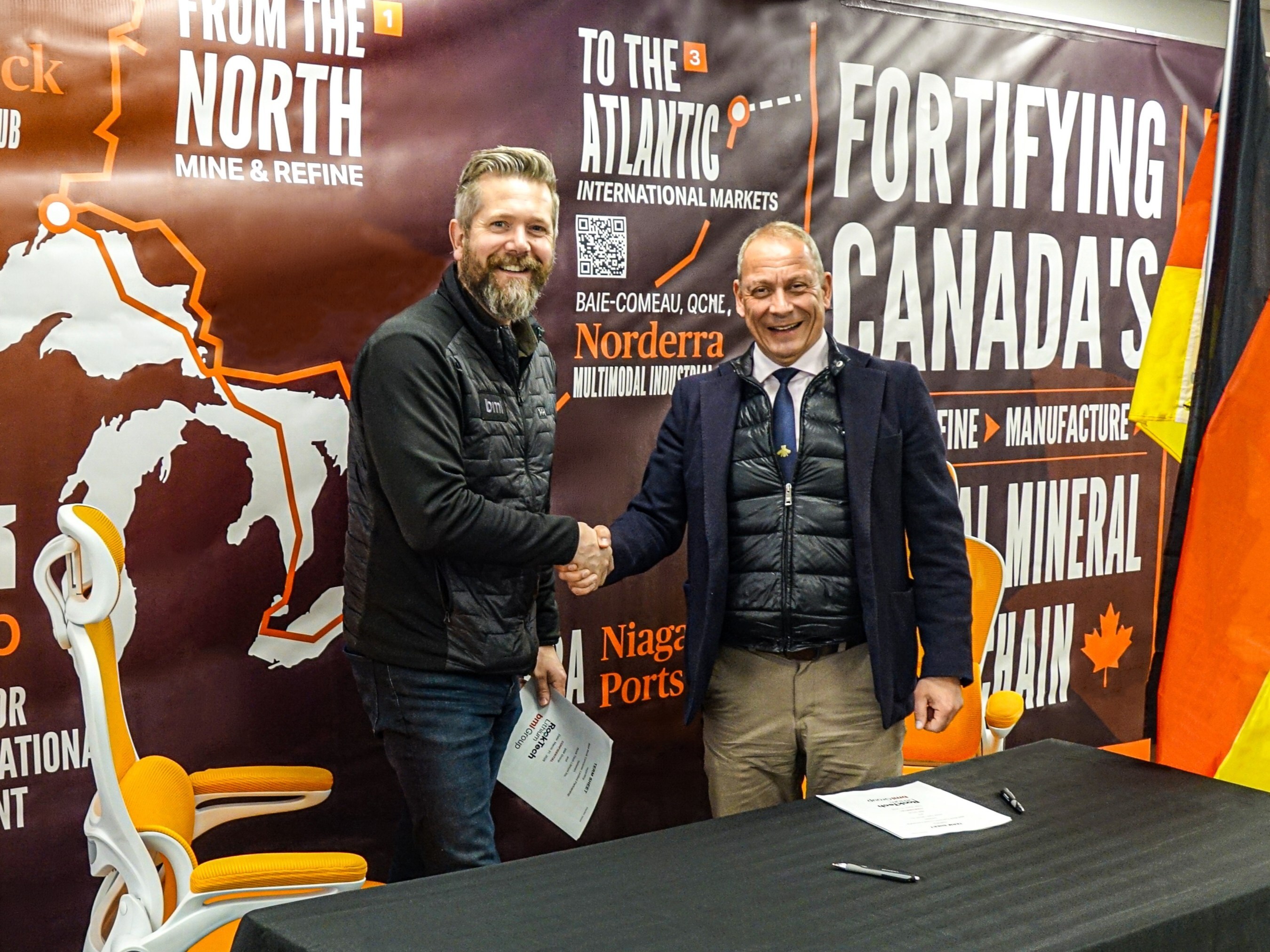 Two men shake hands at a mining industry trade show with Norderra and Niagara Ports branding visible in background.