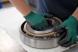 Worker in green gloves inspecting a large industrial ball bearing with metallic rings on white surface