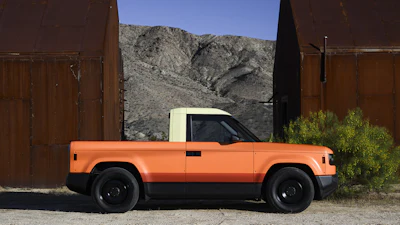 Orange pickup truck parked between rusted metal structures with desert mountains in background