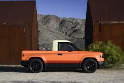 Orange pickup truck parked between rusted metal structures with desert mountains in background