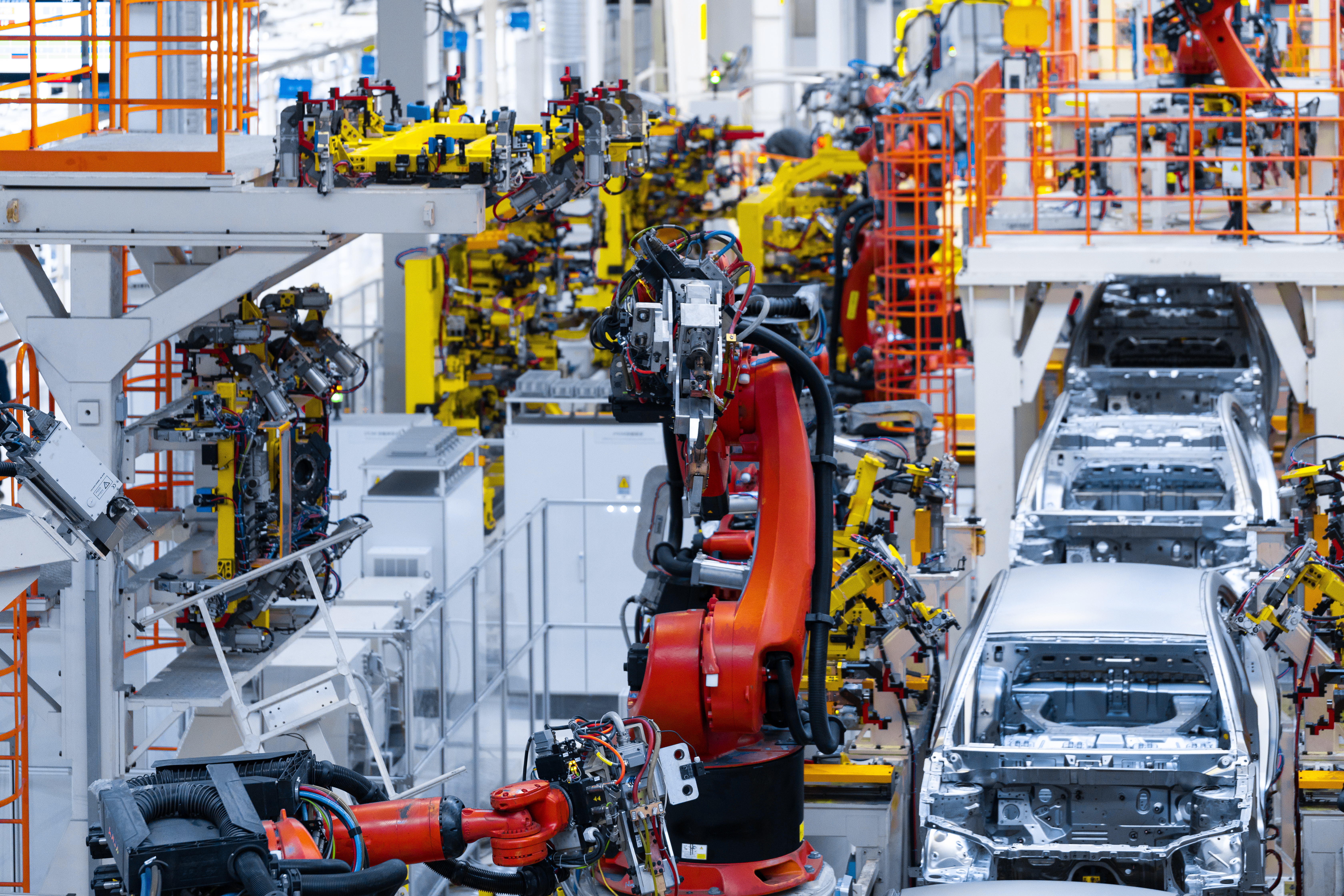 Automotive assembly line with yellow robotic arms and red welding equipment manufacturing vehicles on factory floor