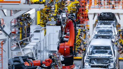 Automotive assembly line with yellow robotic arms and red welding equipment manufacturing vehicles on factory floor
