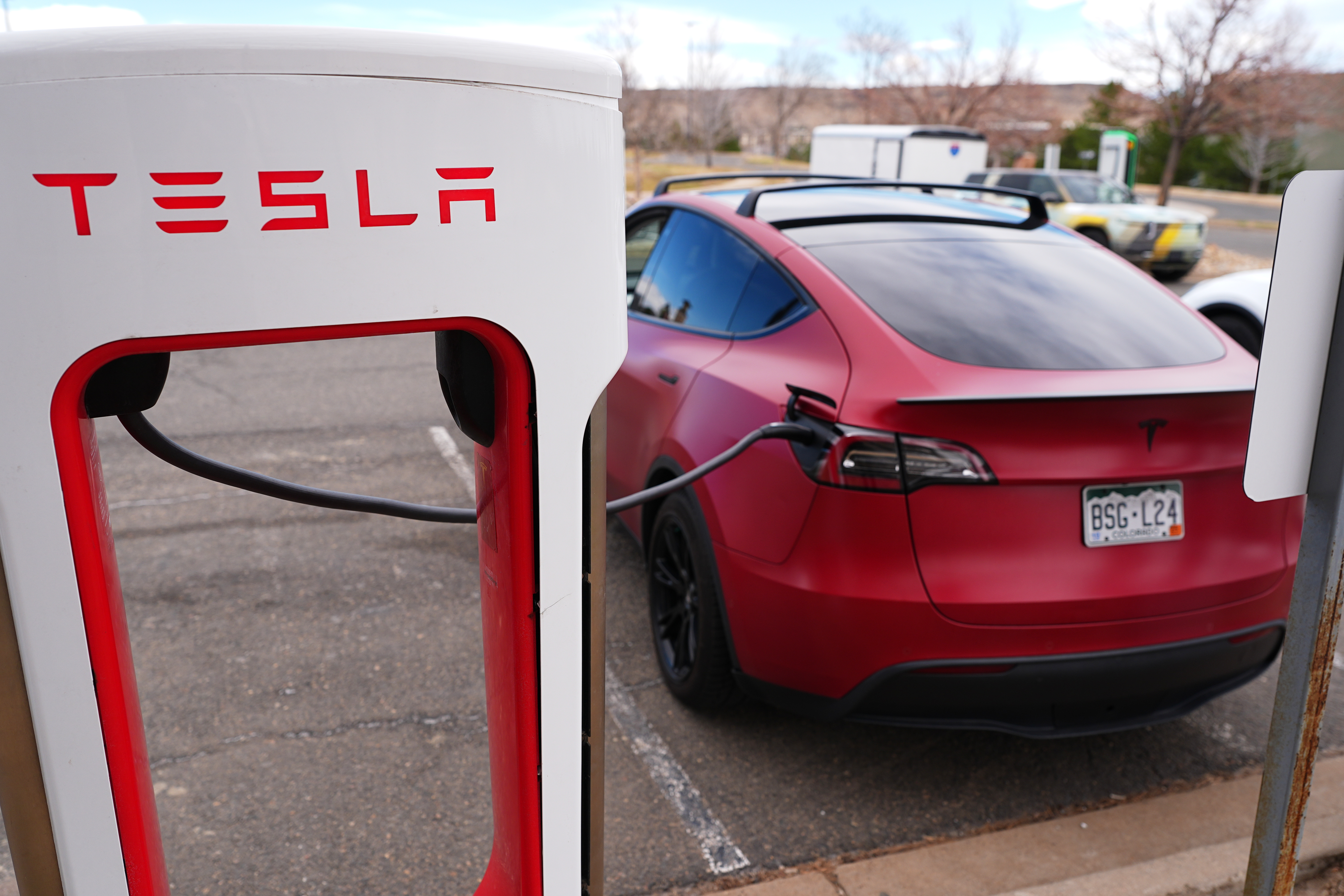 Red Tesla Model 3 charging at Tesla Supercharger station with red and white branding