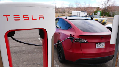 Red Tesla Model 3 charging at Tesla Supercharger station with red and white branding