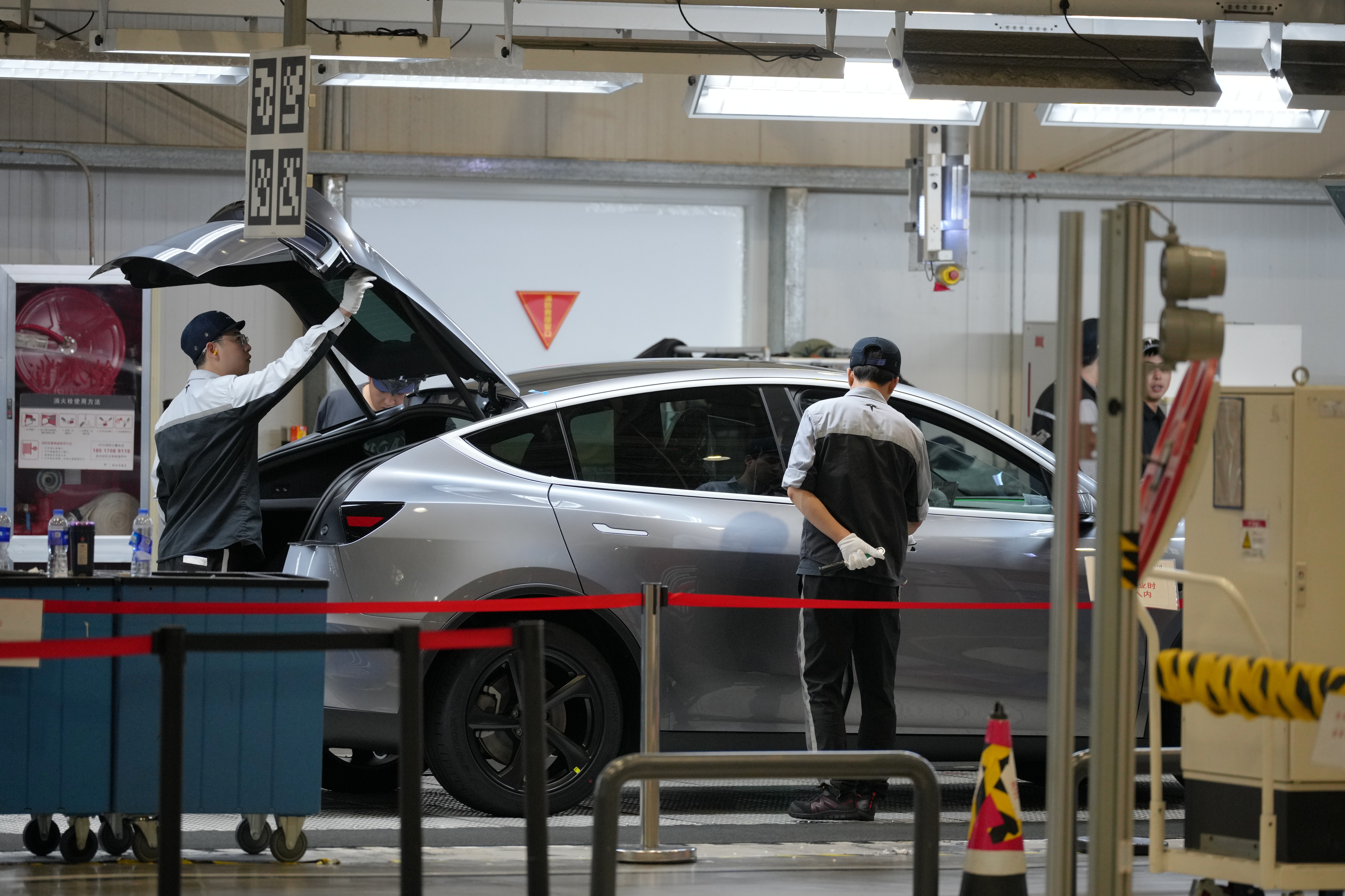 Technicians servicing a silver vehicle in an automotive repair facility with tools and equipment visible
