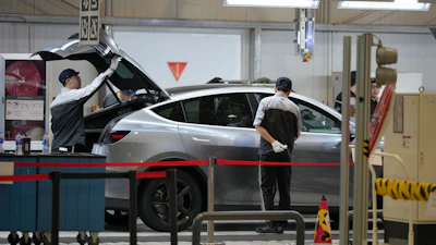 Technicians servicing a silver vehicle in an automotive repair facility with tools and equipment visible