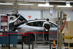 Technicians servicing a silver vehicle in an automotive repair facility with tools and equipment visible