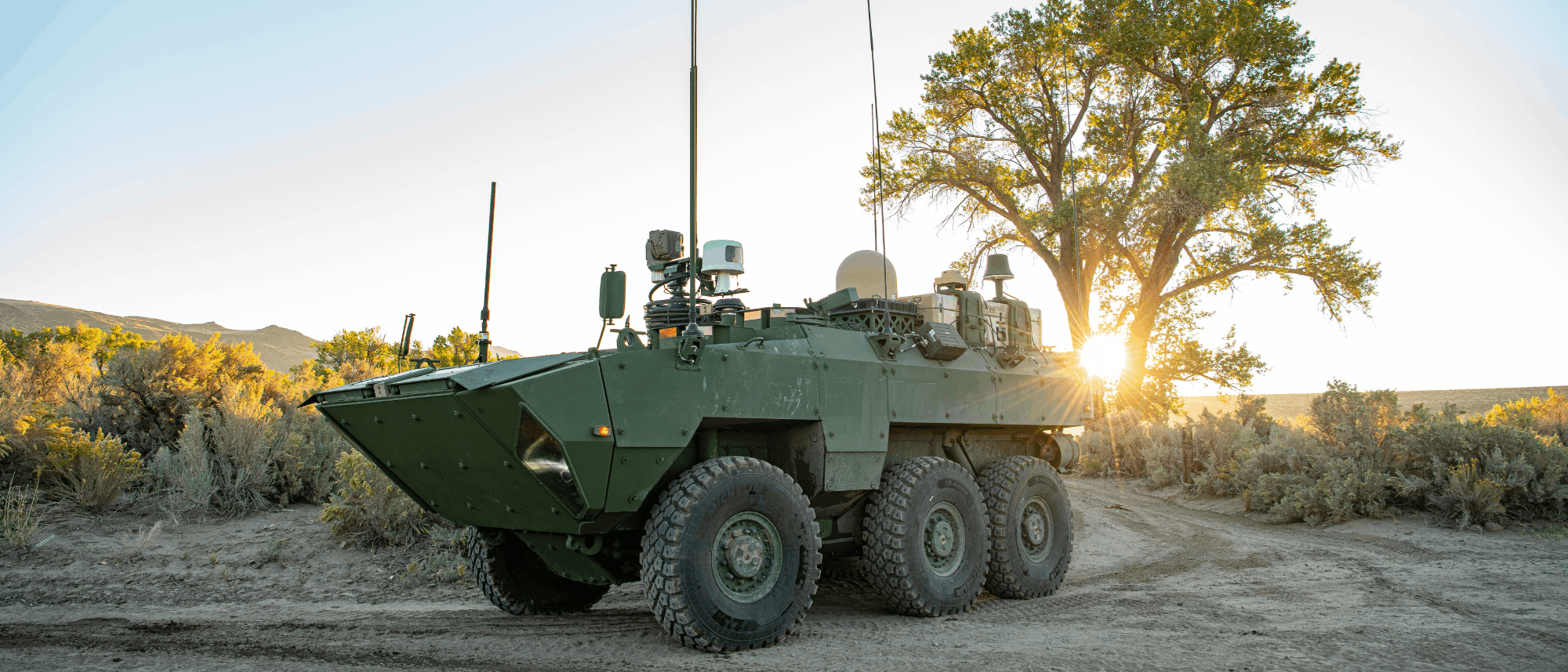 Military armored personnel carrier positioned in desert terrain at sunset with sparse vegetation